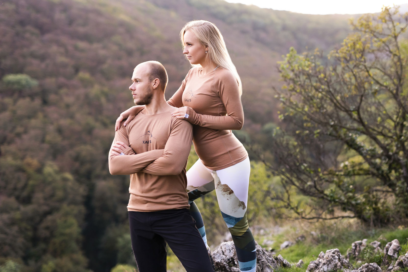 Ein Paar - Frau und Mann stehen aufm Berg bei Sonnenuntergang. Beide haben ein langarmiges Merino Tshirt der Marke KALLYS an.