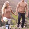 Ein Paar - Frau und Mann - machen eine Bergwanderung. Halten die Hände und haben braunes Merino Langarmshirt der Marke KALLYS an.